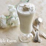 homemade vanilla bean keto milkshake in a tall glass with spoons and white flowers